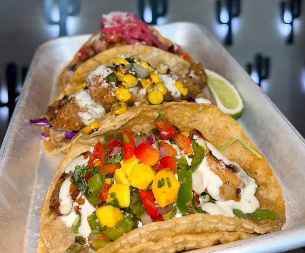 Three colorful tacos with diverse fresh toppings in a metal tray.