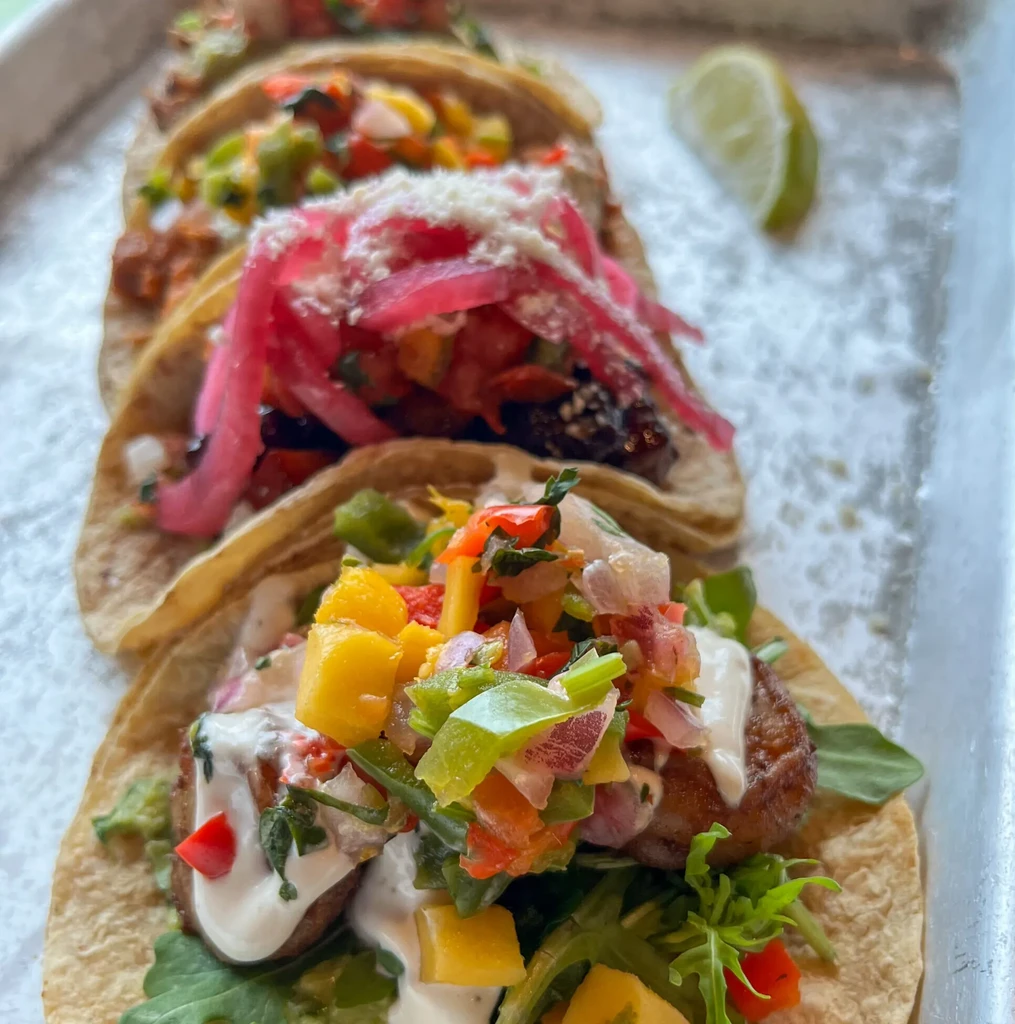 Four fresh tacos with colorful toppings served on a light tray.