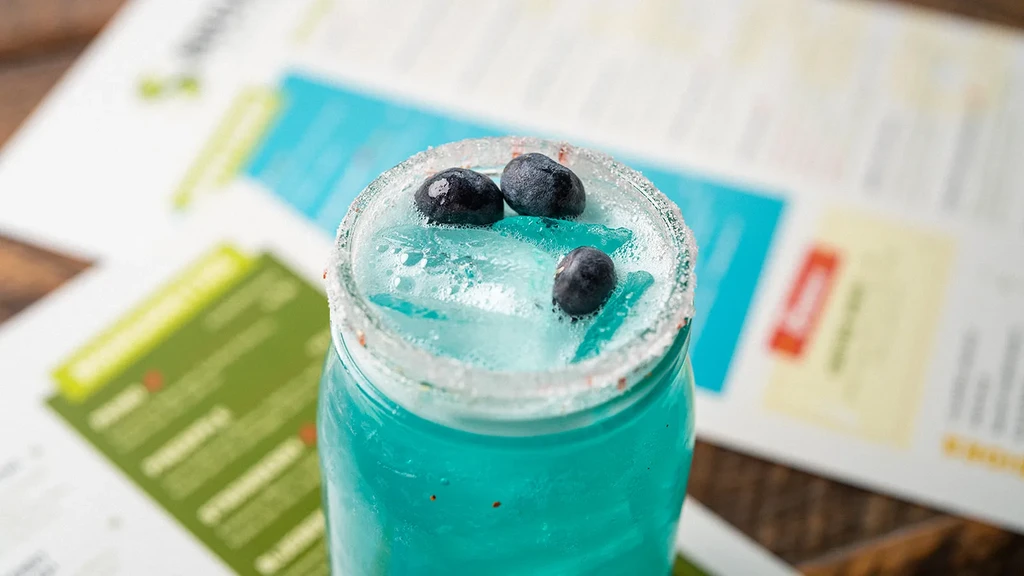 Blue drink in a jar with blueberries, ice, and a white rim.