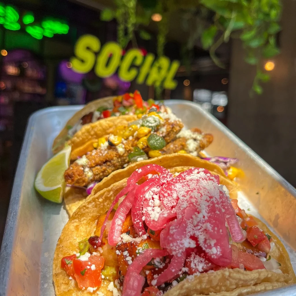 Three vibrant, gourmet tacos on a silver tray in a restaurant.