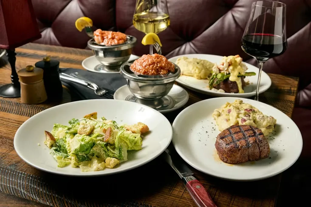 Restaurant table with steak, Caesar salad, steak tartare, and wines.