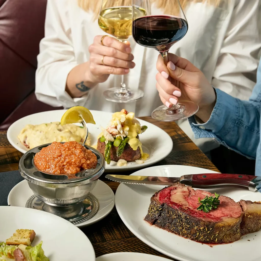 Restaurant dining scene, various gourmet dishes, and two people toasting wine.