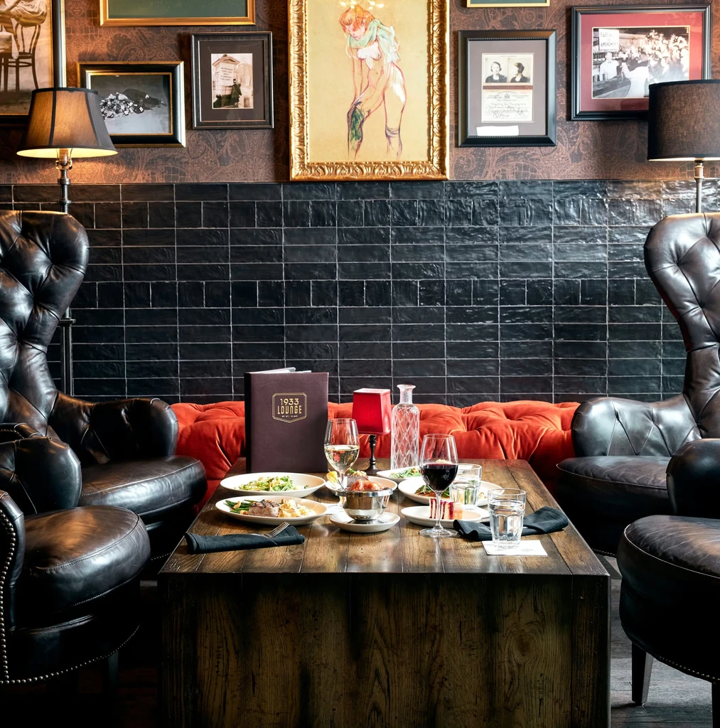 Dark, intimate 1933 LOUNGE with food, wine, and leather armchairs.