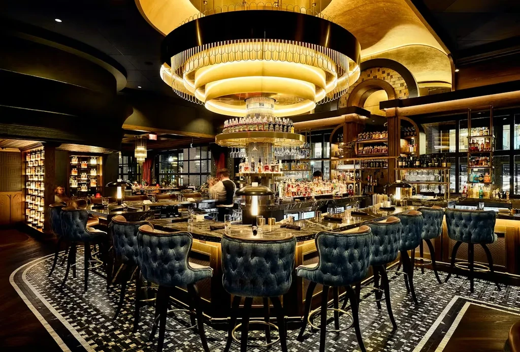Elegant circular bar, glowing gold chandelier, dark stools, stocked spirits.
