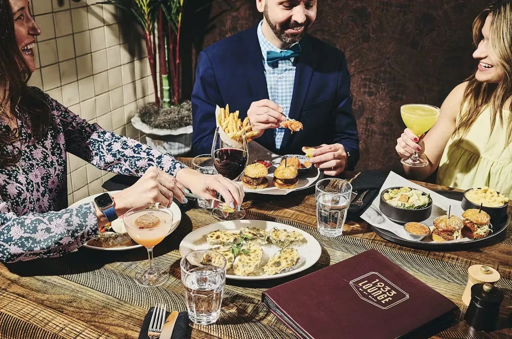 Three smiling guests enjoying food and drinks at 1933 Lounge.