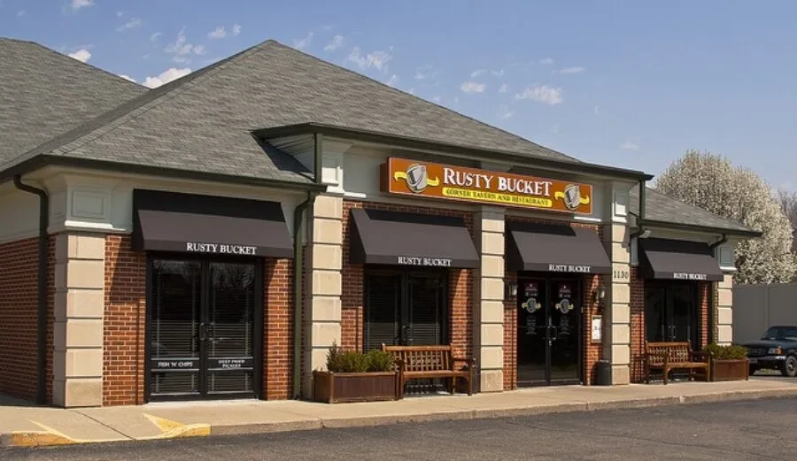 Rusty Bucket restaurant exterior: red brick, stone pillars, gabled roof, awnings.