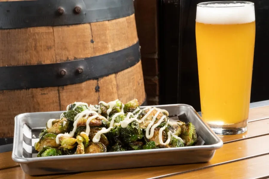 Roasted Brussels sprouts with sauce and beer on a wooden table.
