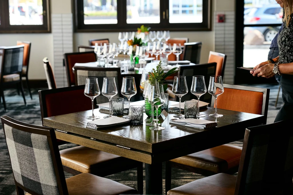 Dark wood restaurant tables set with multiple wine glasses and plants.