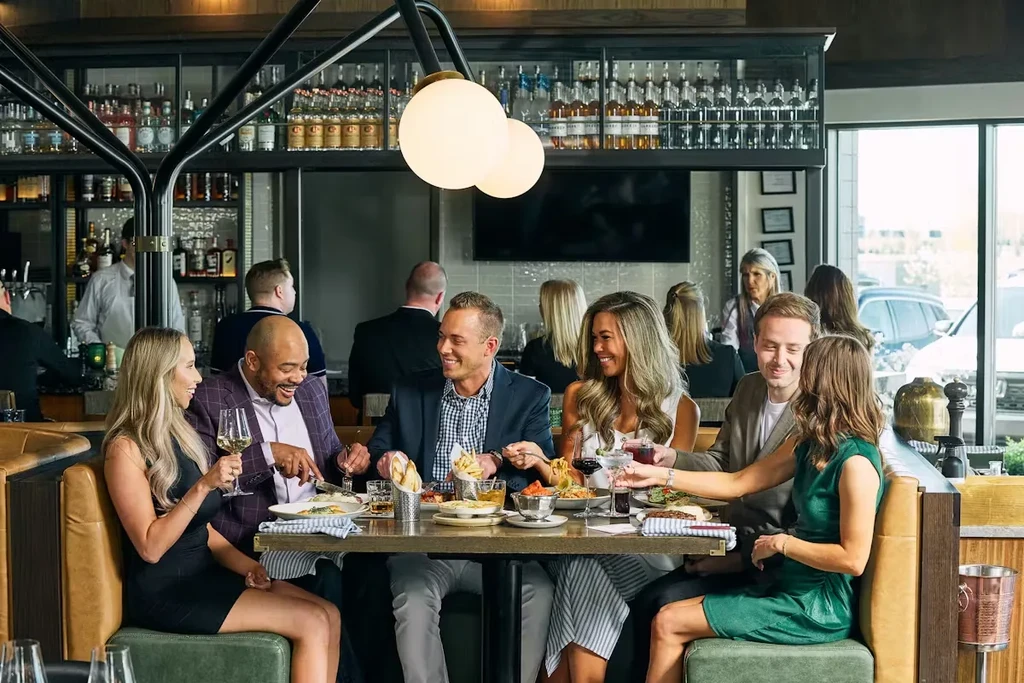 Six smiling adults dining and socializing in a modern restaurant.
