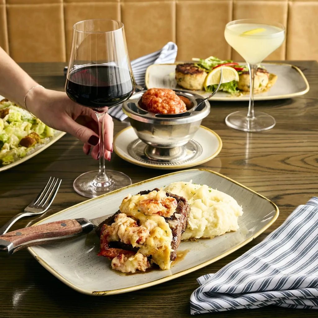 Restaurant table displaying plated steak, crab cakes, wine, and cocktails.