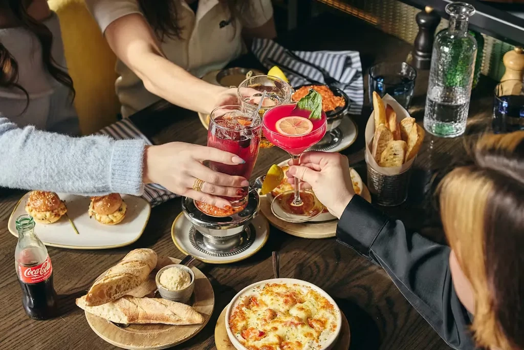 Overhead: Hands toasting colorful drinks and food on a restaurant table.