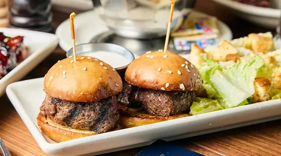 Two sesame bun beef sliders with a side salad.