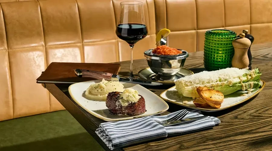 Restaurant table with seared meat, mashed potatoes, Caesar salad, and wine.