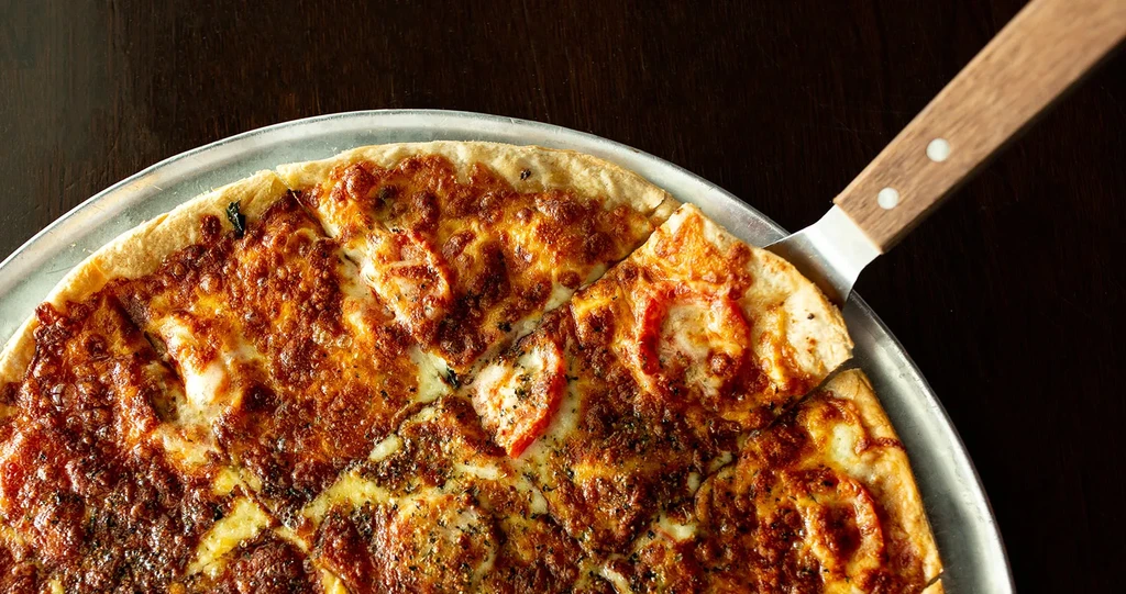 Freshly baked pizza with cheese and tomatoes, a slice being lifted.