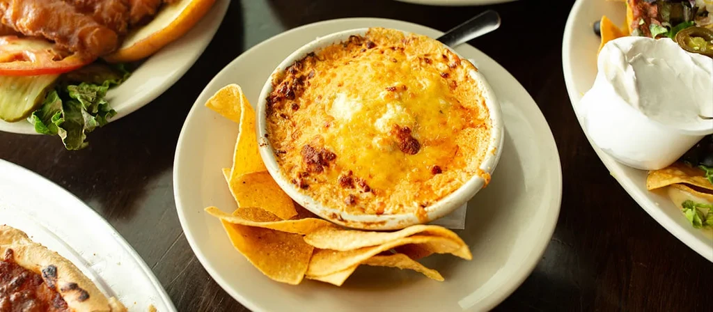 Bubbling cheesy dip and tortilla chips surrounded by other restaurant dishes.