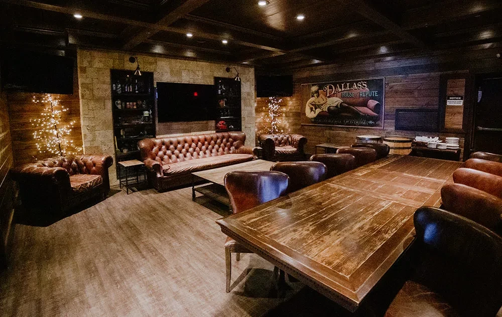 Warmly lit private lounge with dark wood, leather sofas, vintage poster.