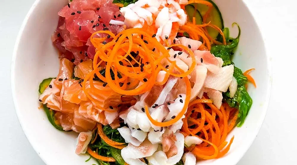Poke bowl with diced tuna, salmon, white seafood, vegetables, sesame seeds.