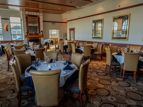 Upscale restaurant dining room with set tables, fireplace, and patterned carpet.
