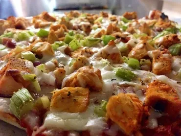 Close-up of pizza with cheese, chicken, and green diced vegetables.