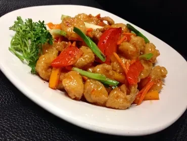Close-up of sweet and sour chicken/shrimp with vegetables and herb garnish.
