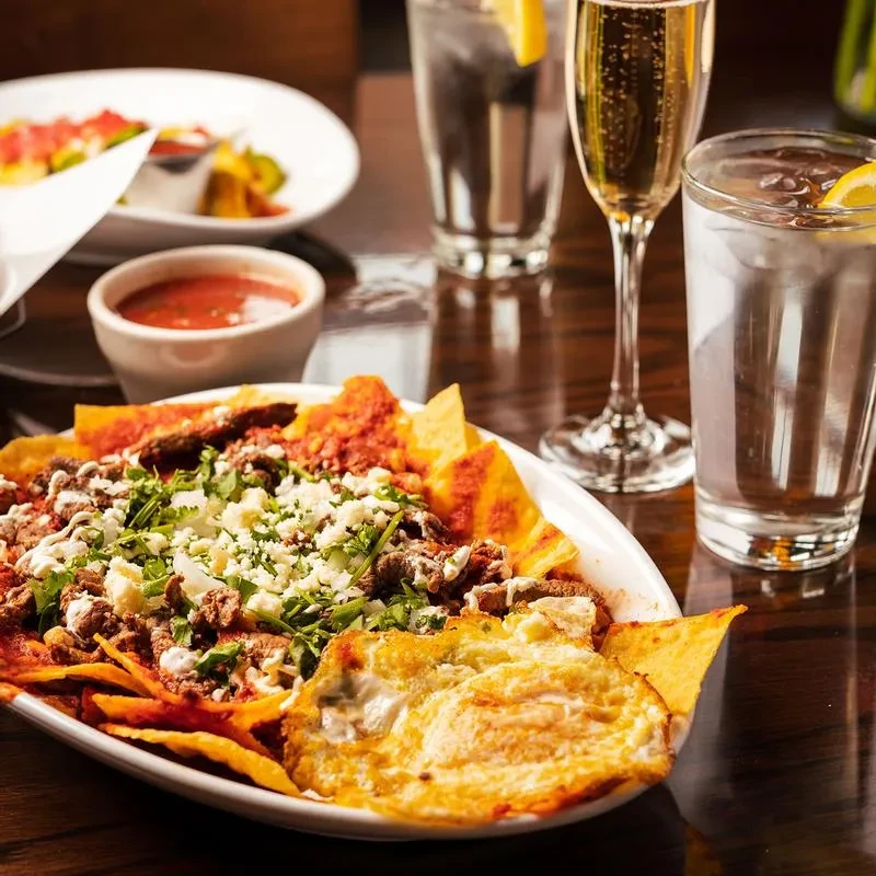 Restaurant table with chilaquiles, fried eggs, salsa, and multiple drinks.