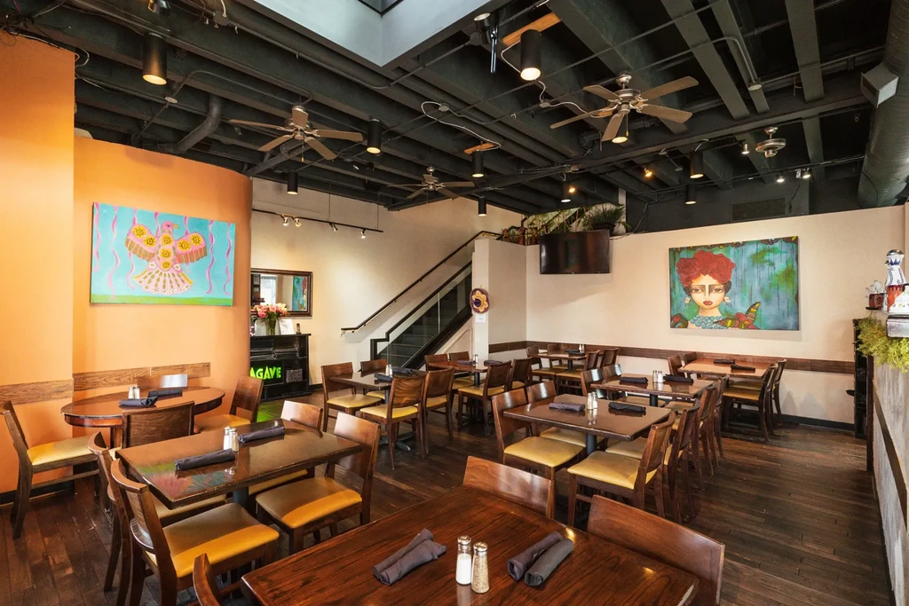 Spacious modern restaurant interior with wooden tables, colorful art, and AGAVE sign.