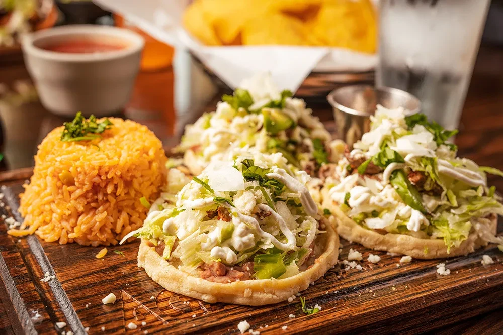 Close-up of three Mexican sopes with rice on a wooden board.