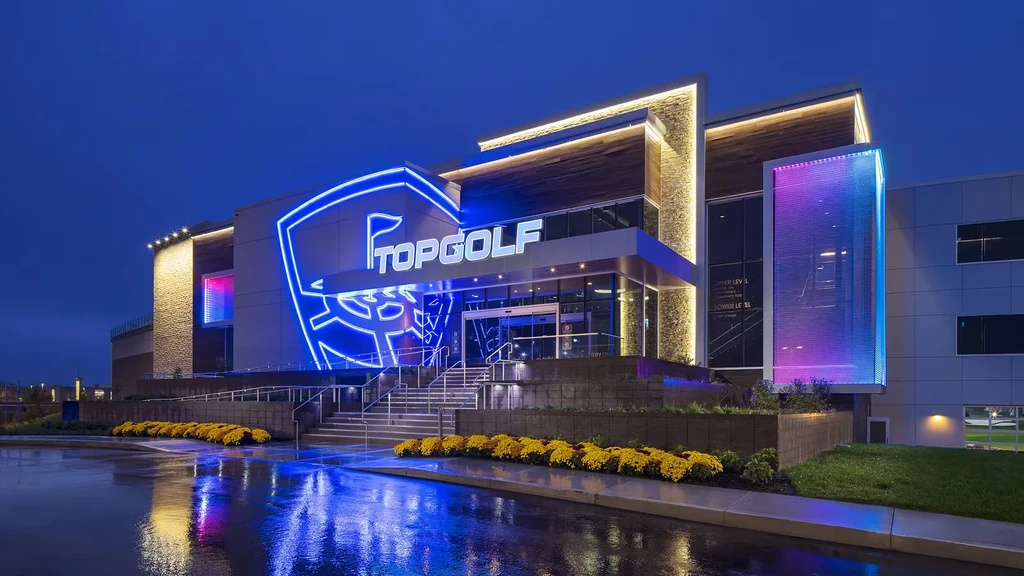 Modern Topgolf building at night, illuminated by blue neon and accent lights.
