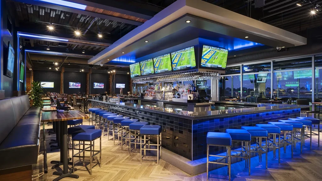 Modern bar interior, blue lighting, TVs showing football, TopGolf branding.