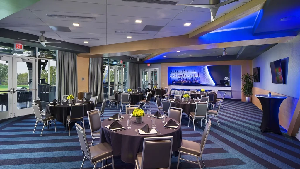 Modern event room with round tables, blue-lit bar, and outdoor lawn view.