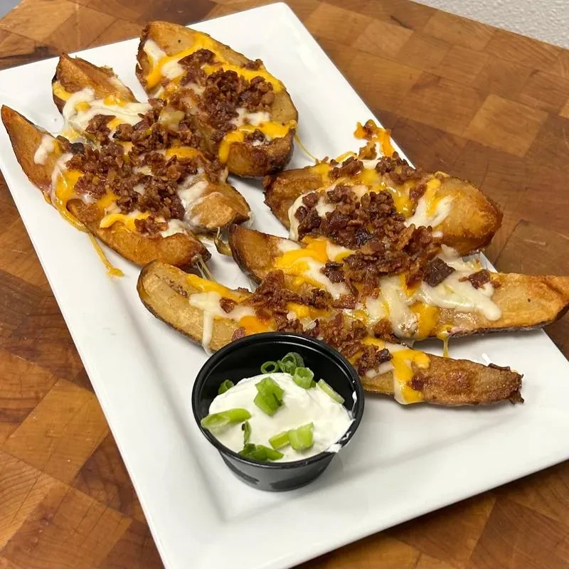 Five cheesy bacon potato skins with a side of sour cream.