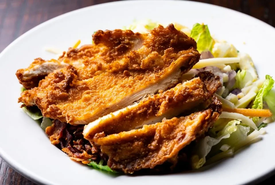 Close-up of sliced crispy fried chicken with a vibrant salad.