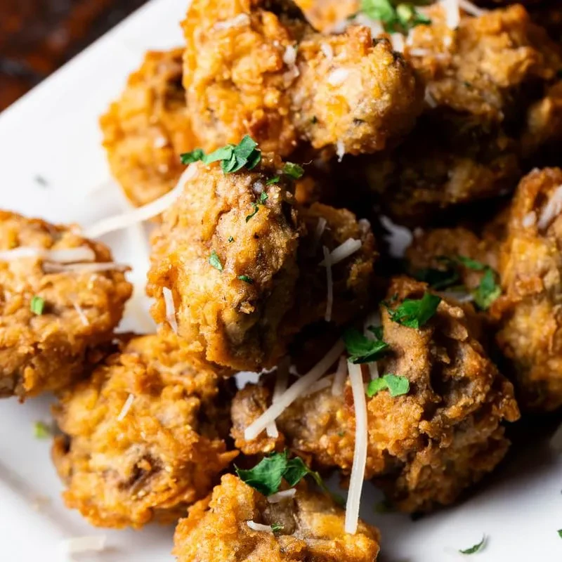Piled fried nuggets with golden batter, cheese, and green herbs.