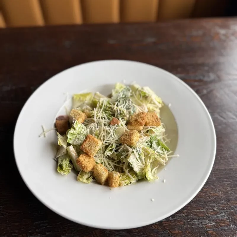 Close-up Caesar salad with romaine, Parmesan, and croutons on a wooden table.