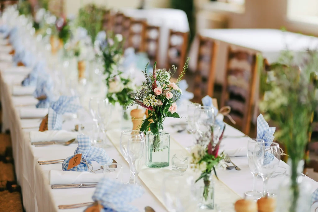 Meticulously set long dining table with gingham napkins and delicate floral arrangements.