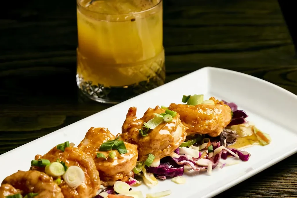 Five golden-brown shrimp in creamy sauce on cabbage with a cocktail.