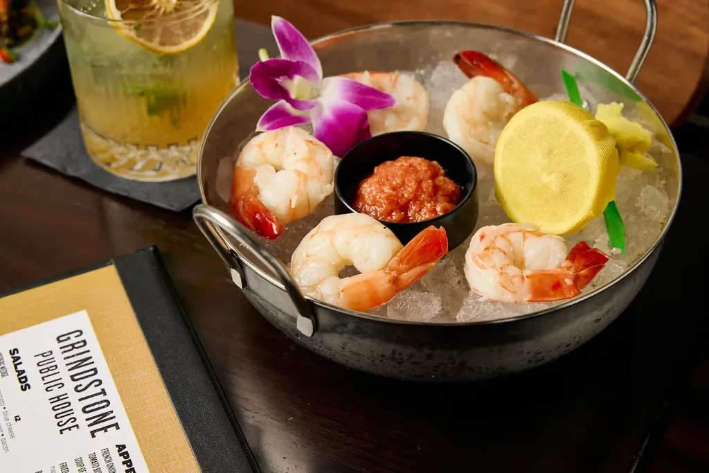 Shrimp cocktail with orchid garnish, beverage, and menu at Grindstone Public House.