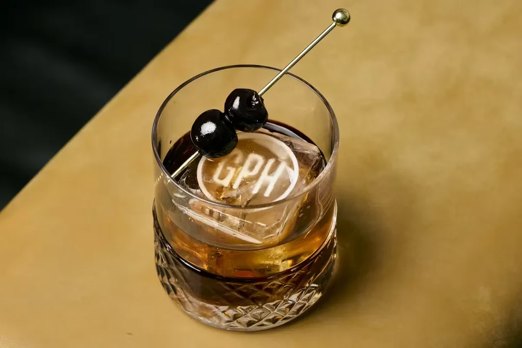 Whiskey cocktail with monogrammed 'GPH' ice cube and cherry garnish.