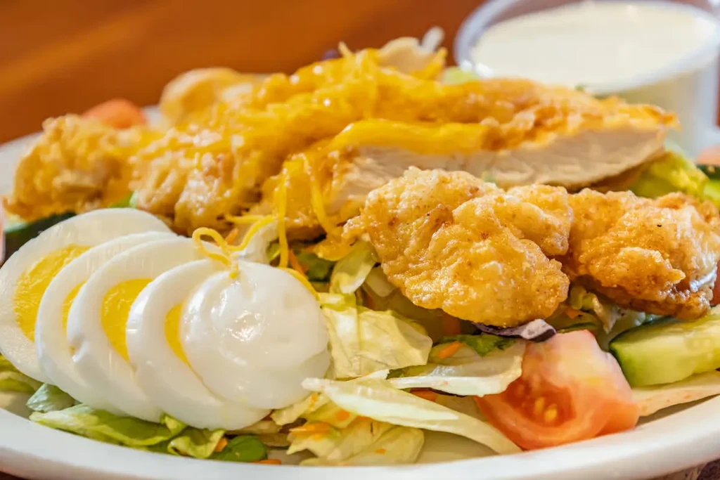 Salad with fried chicken, hard-boiled eggs, shredded cheese, and mixed greens.