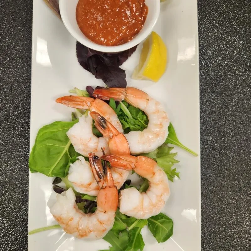 Shrimp cocktail on rectangular plate with sauce, lemon, and lettuce.