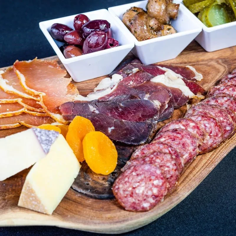 Well-arranged charcuterie board with meats, cheeses, olives, pickles, and apricots.