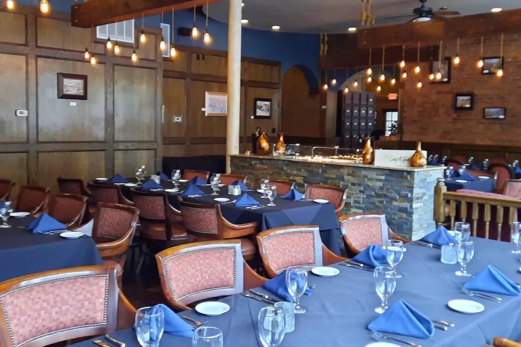 Empty restaurant dining room with brick, wood walls, and warmly lit tables.