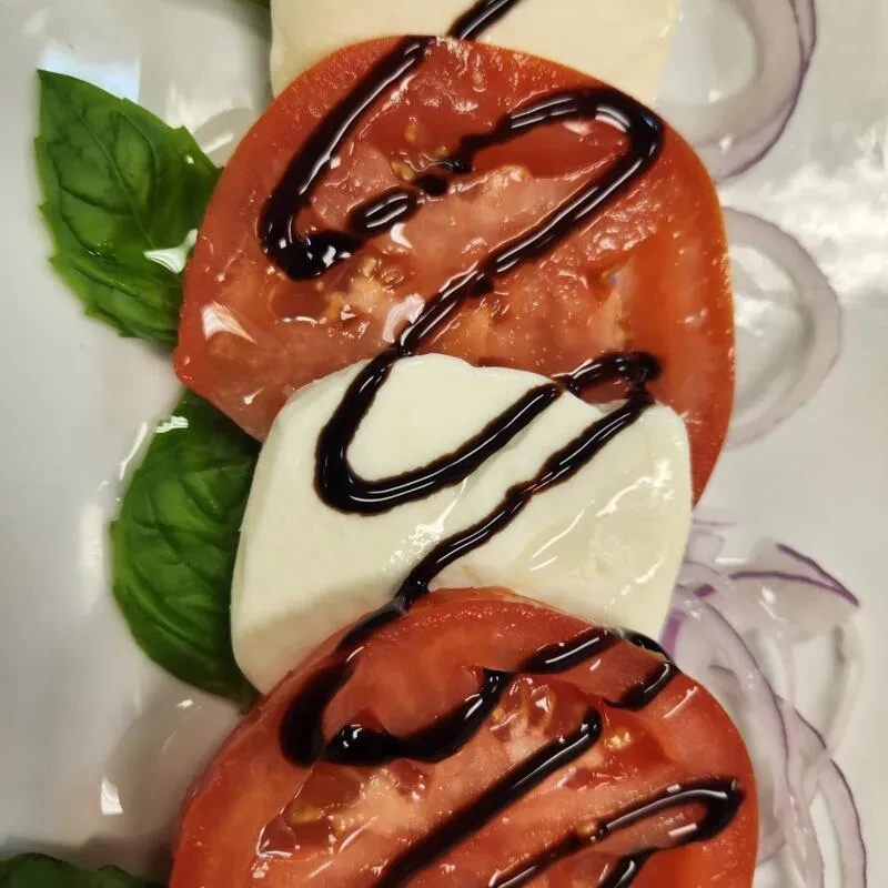 Fresh Caprese salad with tomatoes, mozzarella, basil, balsamic glaze, and onion.