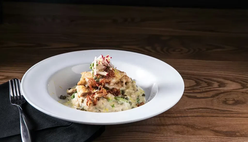 Pan-fried fish with creamy base, capers, and vegetables on white plate.