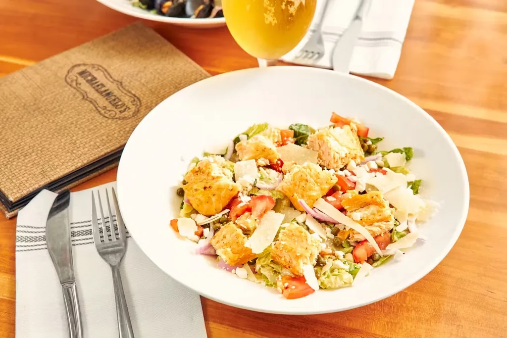 Large salad with chicken/salmon, Michaelangelo's menu, and dining setting.