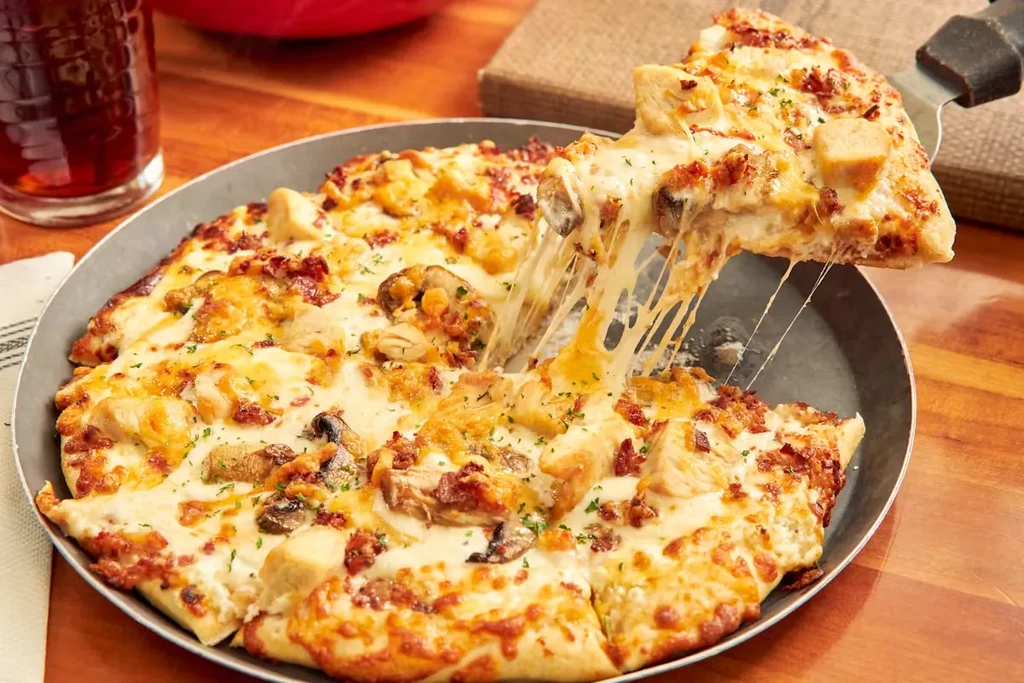 Pizza slice lifted from pan, long cheese pull, chicken and mushroom.