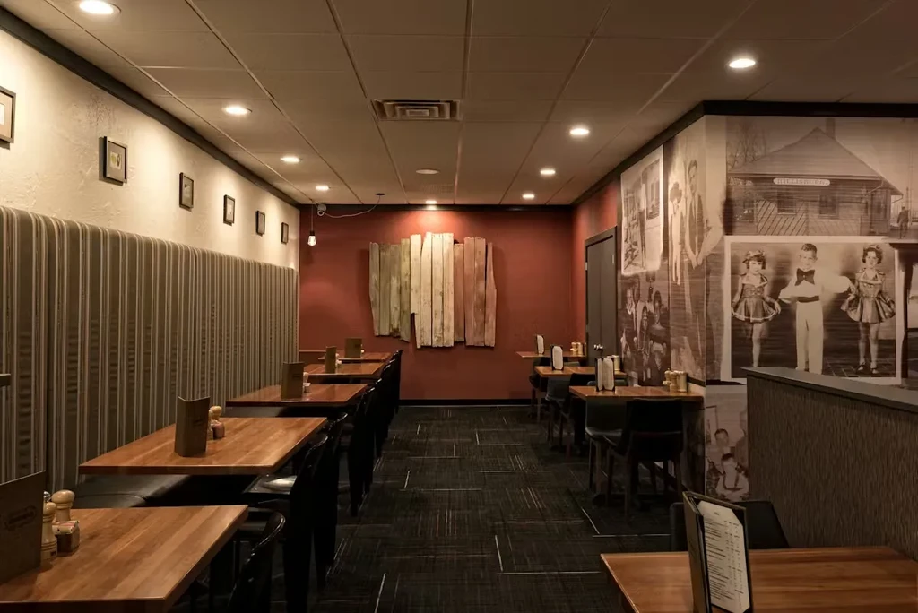 Warm, empty restaurant with banquettes, wooden tables, and historical murals.