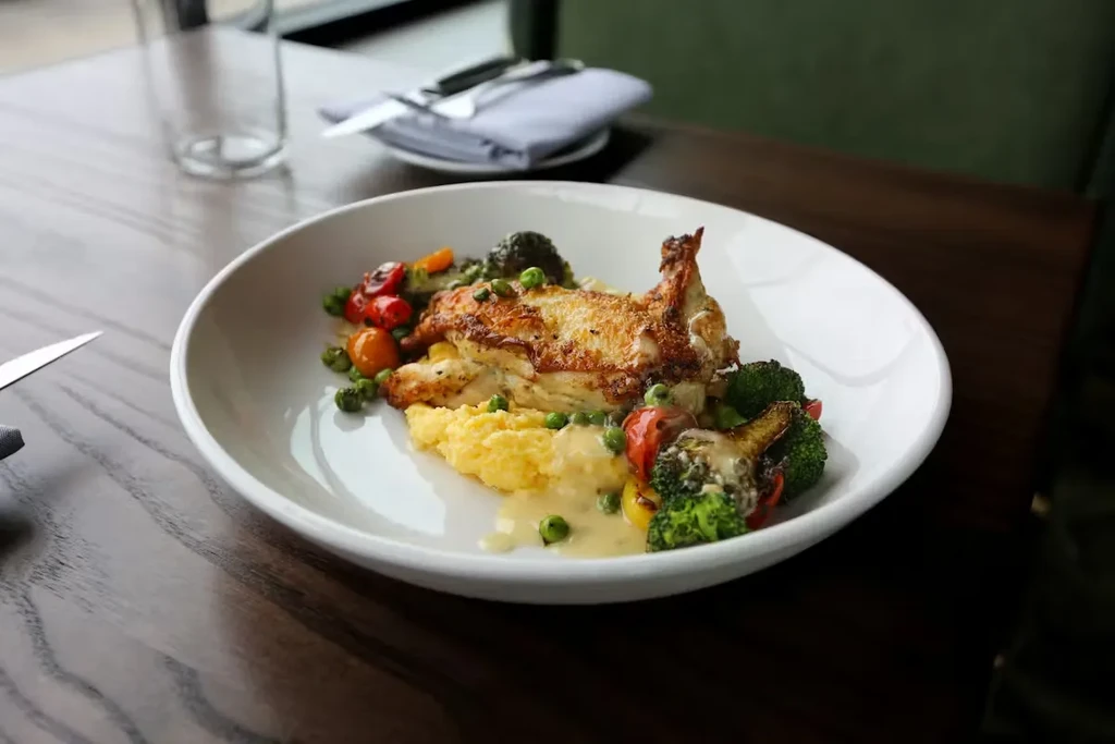 Golden-brown chicken, yellow mashed potatoes, colorful vegetables with creamy sauce.
