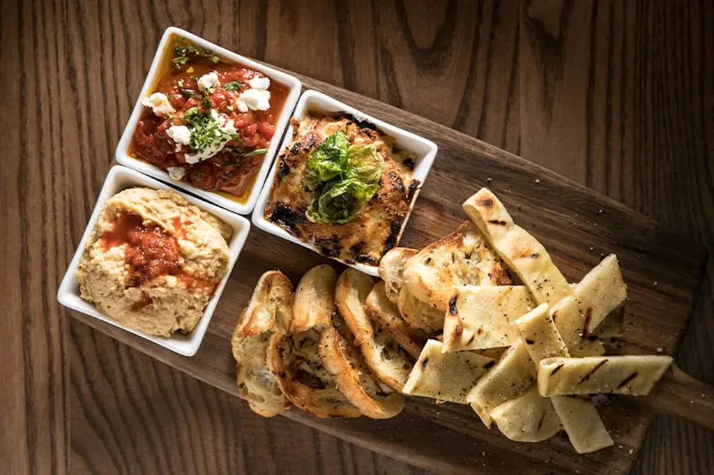 Three assorted dips and breads on a rustic wooden board.