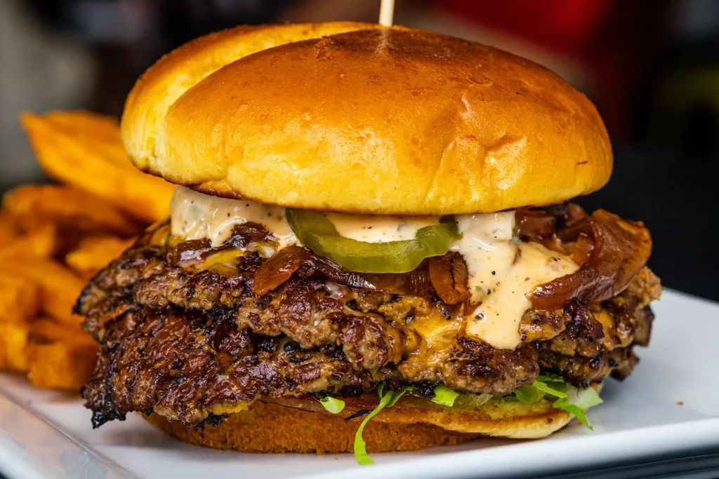 Close-up double smash burger with melted cheese, onions, and jalapeño.